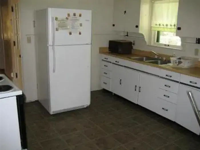 Kitchen with full size fridge with upper freezer, microwave next to metal sink with dish rack across from electric stove.