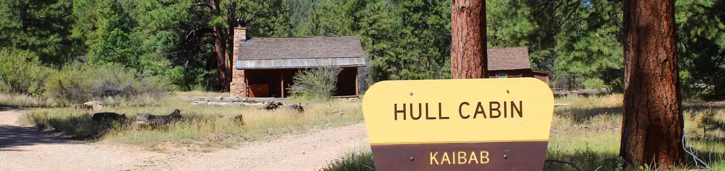 A yellow and brown Forest-Service sign identifies Hull Cabin on the Kaibab National Forest in the foreground. The cabin is visible in the background.