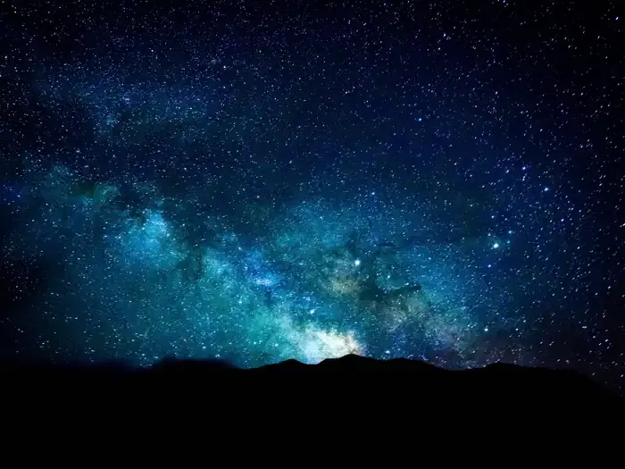 Night sky with the Milky Way over dark sand dunes.