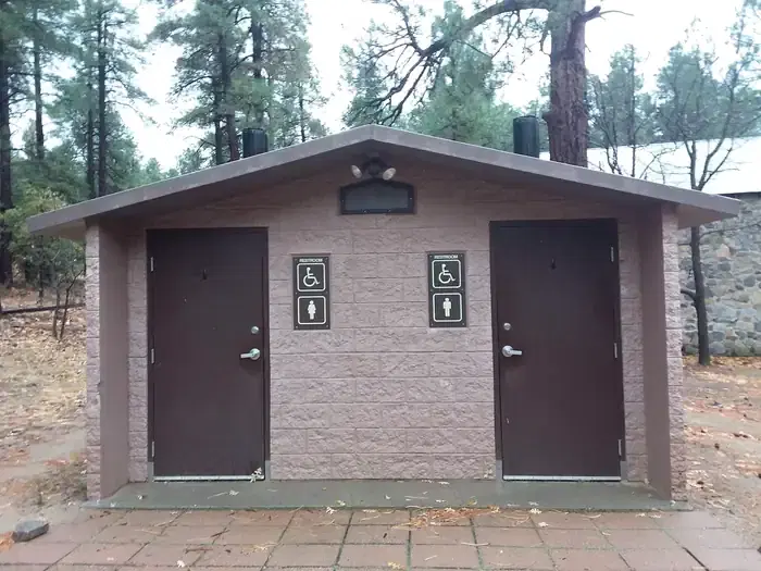 Accessible two vault toilet building with concrete slab in front located behind main building.
