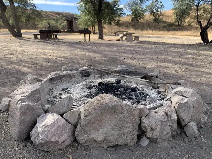 A stone-ringed fire pit on the ground with dark ashes in the center.
