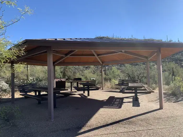 Large covered ramada with 3 picnic tables, benches, a grill and trashcans