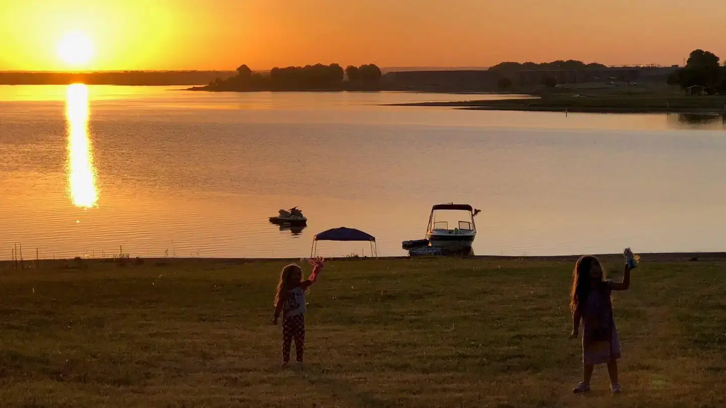 Two children stand near the shore of a lake at sunset