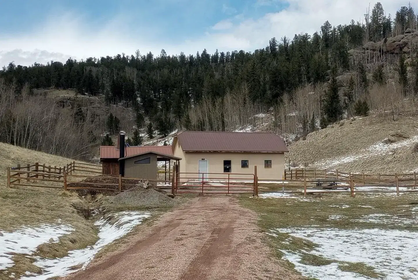 Front side of guard station, with fenced yard, outhouse, picnic table and fire ring.